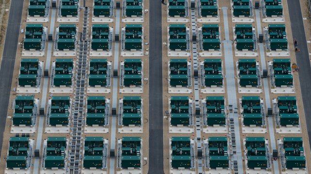 Aerial view of a large-scale battery energy storage system facility featuring rows of green containers on gravel pads with paved access paths in Faversham, England, United Kingdom.