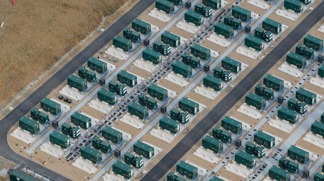 Aerial view of a large-scale battery energy storage system with rows of green containers on concrete pads and gravel paths in Faversham, England, United Kingdom.