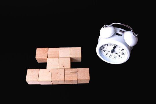 Blank wooden blocks and white analog alarm clock on black background