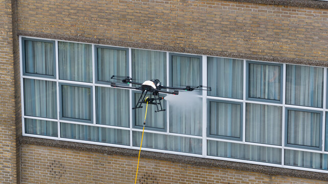 Aerial view of a professional drone cleaning the glass windows of a brick building with a high-pressure water spray in Amersfoort, Utrecht, Netherlands.