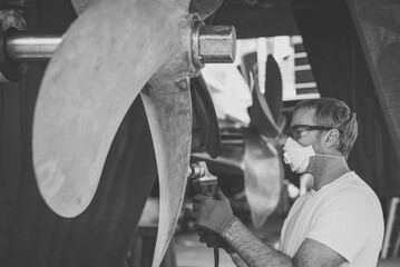 Caucasian male superyacht deckhand engineer polishing a yacht propeller with a power tool, gloves, mask and eye protection glasses  © lupiphoto