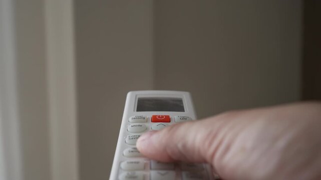 Hand adjusting air conditioner settings with remote control at home, illustrating temperature management, energy consumption, cooling efficiency and sustainable household climate control