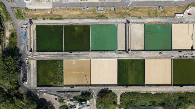 Aerial view of a water treatment facility with rectangular filtration tanks containing water of varying shades of green and beige, in Reading, England, United Kingdom.