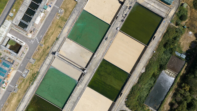 Aerial view of rectangular water treatment tanks with varying green and beige filtration beds separated by concrete walkways at a facility in Reading, England, United Kingdom.