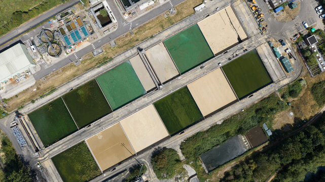 Aerial view of a wastewater treatment plant featuring rectangular sedimentation tanks with varying shades of green and beige water in Reading, England, United Kingdom.