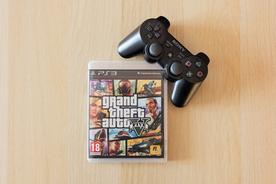 DRESDEN, GERMANY - 19. August 2026: GTA V game with a Playstation controller. Grand Theft Auto 5 from Rockstar Games lying on a table. Close-up of the videogame cover in the case.