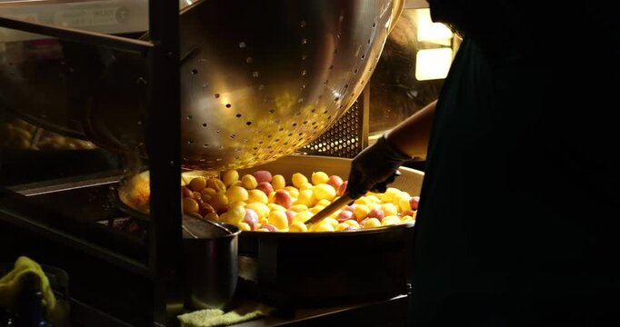 Side view slow motion shot from behind street vendor stirring large batch of traditional deep-fried sweet potato balls at Ningxia Night Market in Taipei. Cook uses large utensil to toss balls