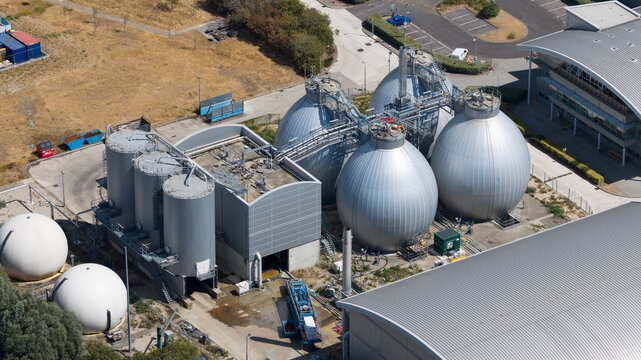 Aerial view of a modern industrial wastewater treatment facility featuring large spherical digester tanks and cylindrical storage units in Reading, England, United Kingdom.
