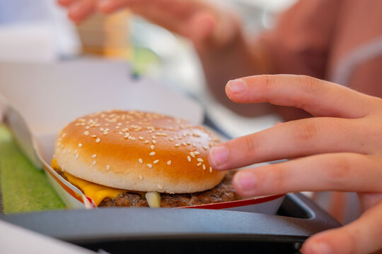 sesame seed burger held in hands, teenager person holding delicious hamburger, fast food cafe snack, sensory pleasure eating, appetite unhealthy lunch break outdoors, tasty snack option, takeaway food