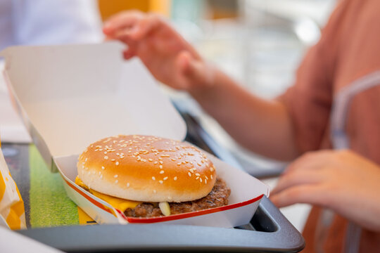 sesame seed burger held in hands, teenager person holding delicious hamburger, fast food cafe snack, sensory pleasure eating, appetite unhealthy lunch break outdoors, tasty snack option, takeaway food