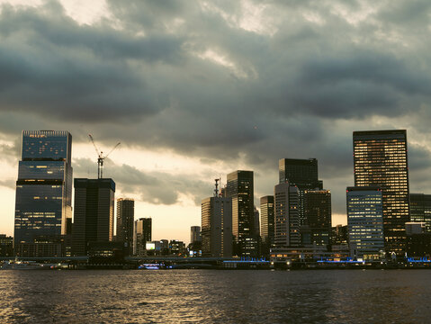 Modern city skyline with illuminated skyscrapers under a dramatic cloudy sky at dusk in Tokyo, Japan