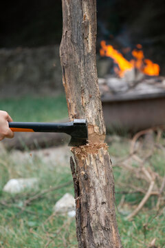 a person's hand using a hatchet to chop a log in front of a burning campfire in nature, concept of bushcraft, concept of survival, concept of camping