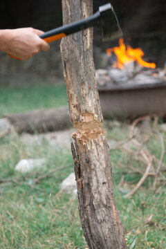 a person's hand using a hatchet to chop a log in front of a burning campfire in nature, concept of bushcraft, concept of survival, concept of camping