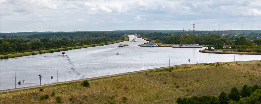 Cargo barge navigates broad Mittellandkanal near Magdeburg, surrounded by green countryside and canal infrastructure. Aerial view shows inland shipping, vessels, waterways and distant wind turbines