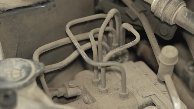A close up of dusty metal brake lines in car engine.