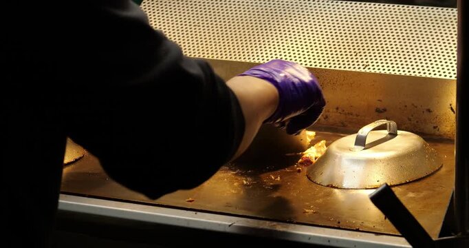 Close up rear side view shot of vendor preparing thick chunks of meat on flat-top teppanyaki griddle at Asian night market stall. cook uses two metal spatulas to flip and chop sizzling food pieces