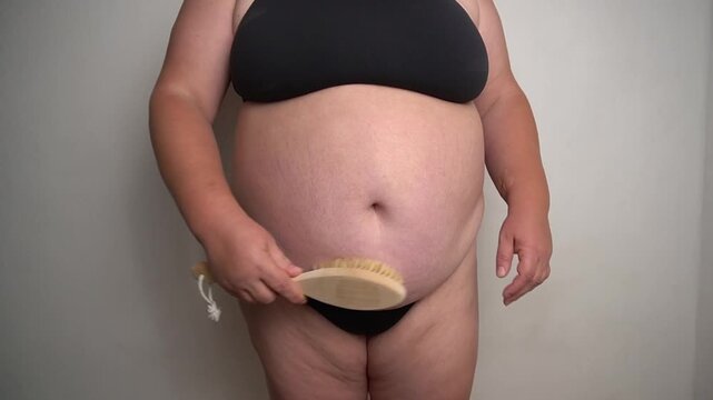 An overweight woman performs a dry brush abdominal massage; the concept of dry brush massage, a body care procedure, a wellness practice, skin peeling.