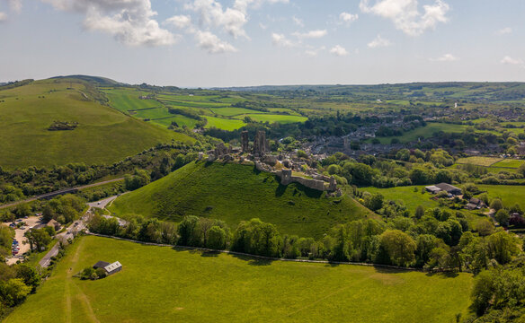 Aerial view of the historic Corfe Castle ruins situated on a prominent green hill surrounded by the lush Purbeck countryside in Corfe Castle, England, United Kingdom.