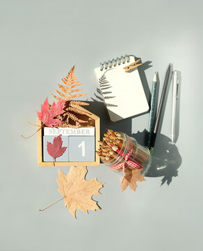 September calendar. Wooden calendar block with date 1 September, pencils, fallen leaves, empty notepad on grey background. top view. copy space. Template for design