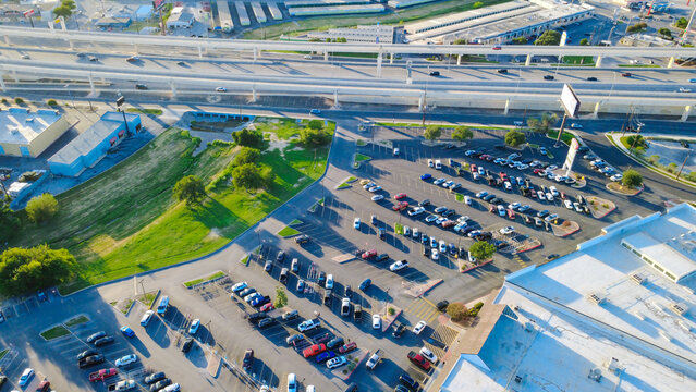 Expansive retail parking lots, parked consumer vehicles sit along Loop 410 near Evers Road. Commercial shopping plazas border multi level highway overpasses across San Antonio, Texas
