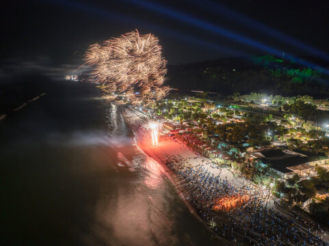 Aerial view of fireworks exploding over the beach at Marina Palmense at night, with crowds gathered along the coastline and illuminated beach facilities in Fermo, Marche, Italy.