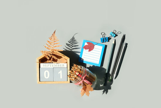 September calendar. Wooden calendar block with date 1 September, fallen dry leaves, pencils, empty note on grey background. flat lay. copy space. Template for design