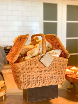 Rustic woven wicker basket filled with assorted fresh bread and pastries displayed on a counter in a warm bakery or caf&eacute; setting. The natural basket texture and freshly baked goods create an inviting 