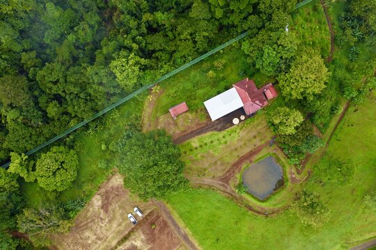 Aerial view of Kapok Hanging Bridges surrounded by lush rainforest, a small pond, and a building with a red roof in La Virgen, Heredia Province, Costa Rica.