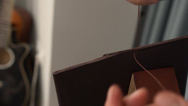 Craftsman hand stitching genuine leather with needle and thread in a workshop creating handmade goods