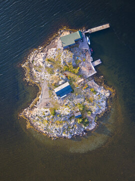 Aerial view of Sando island featuring small wooden cabins, rocky terrain, and a wooden pier extending into the surrounding blue water in Vallda, Hallands lan, Sweden.