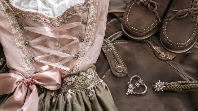 Traditional Bavarian dirndl and lederhosen arranged for Oktoberfest celebration. German folk costume details with embroidered fabric, leather accessories, and festive cultural heritage concept.
