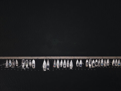Aerial view of sailboats moored along a straight pier in the dark waters of Sando, Vallda, Hallands lan, Sweden.