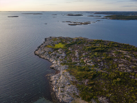 Aerial view of Sando peninsula with rocky terrain, sparse green vegetation, and calm sea under golden hour light in Vallda, Hallands lan, Sweden.