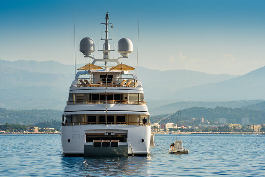 Big white super yacht anchored in the bay of Cannes, in the South of France during summertime with open umbrellas on the top deck for entertainment of charter guests 