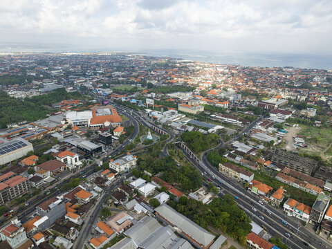 Aerial view of the Statue of Dewa Ruci at a busy intersection in Kuta, surrounded by buildings, trees, and roads leading to the coast. Kecamatan Kuta, Bali, Indonesia.
