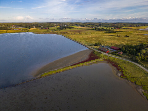 Aerial view of the coastal landscape at Sando with red buildings, green fields, and a road along the water in Vallda, Hallands lan, Sweden.