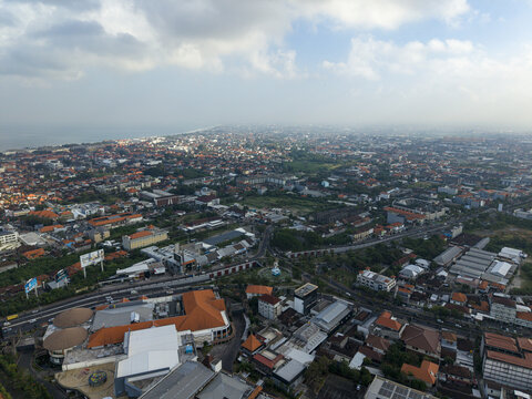Aerial view of the Dewa Ruci statue roundabout surrounded by dense urban development, terracotta rooftops, and roads in Kecamatan Kuta, Bali, Indonesia.
