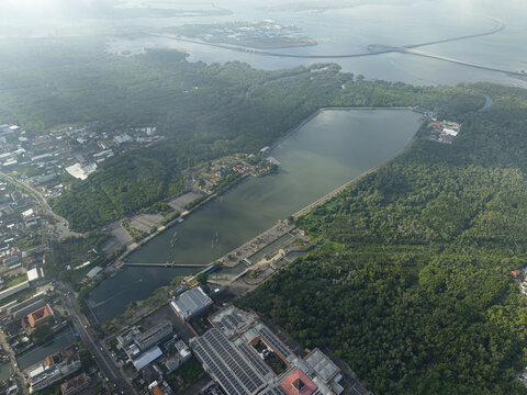 Aerial view of the reservoir near the Statue of Dewa Ruci surrounded by lush mangrove forests and urban infrastructure in Kecamatan Kuta, Bali, Indonesia.