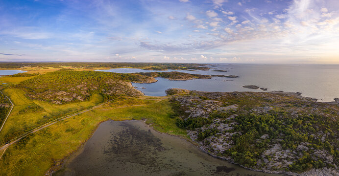 Aerial view of the coastal landscape of Vallda Sando Naturreservat featuring rocky terrain, lush greenery, and calm waters under a soft sunset sky in Vallda, Hallands lan, Sweden.