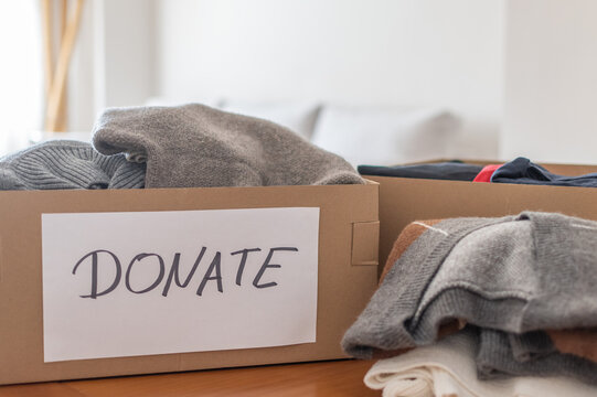 Cardboard box with a donate sign filled with folded clothing items, preparing for charity, reuse, and decluttering in a clean home environment