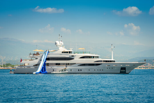 Big white superyacht anchored in the bay of Cannes, south of France during summertime with an inflatable water slide for entertainment of charter guests 