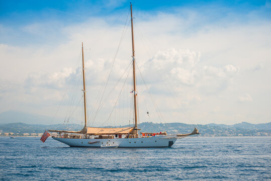 Classic wooden ketch sail yacht, private boat anchored in the bay of Cannes, France with clouds and blue sky, city in the background