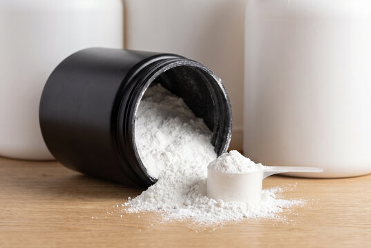 Overturned Black Jar with Creatine Powder and Measuring Scoop on Wood