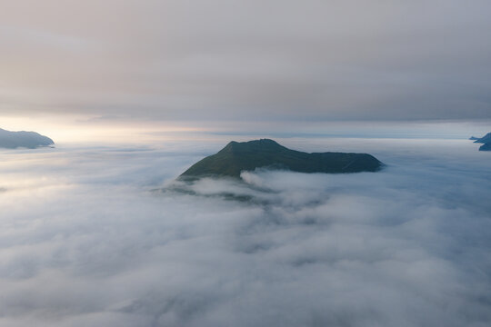 Aerial view of a mountain peak rising above a thick layer of clouds in Unalaska, Alaska, United States.