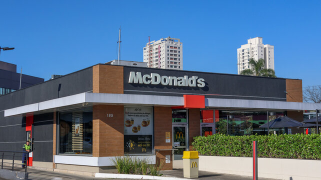 Fachada de restaurante McDonald's em &aacute;rea urbana, com logotipo da rede, entrada comercial, paisagismo e edif&iacute;cios residenciais ao fundo sob c&eacute;u azul. Mogi das Cruzes SP 18 agosto 2026