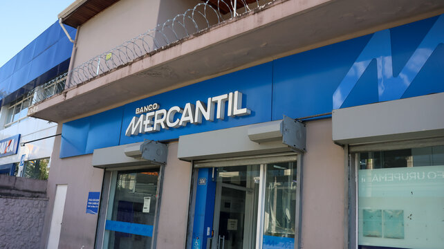 Fachada de ag&ecirc;ncia do Banco Mercantil com letreiro azul, entrada e vitrine, retratando a presen&ccedil;a da institui&ccedil;&atilde;o banc&aacute;ria no com&eacute;rcio da regi&atilde;o do Alto Tiet&ecirc;. Mogi das Cruzes SP 10 Agosto 26