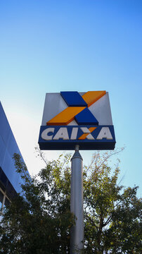 Placa com logotipo da Caixa instalada em frente a uma ag&ecirc;ncia banc&aacute;ria, destacando a identidade visual azul e laranja da institui&ccedil;&atilde;o financeira. Mogi das Cruzes SP 18 agosto 2026