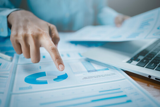 Business report performance evaluation and marketing strategy concept, professional hand pointing pie chart document near laptop analyzing corporate financial data visualization for economic growth