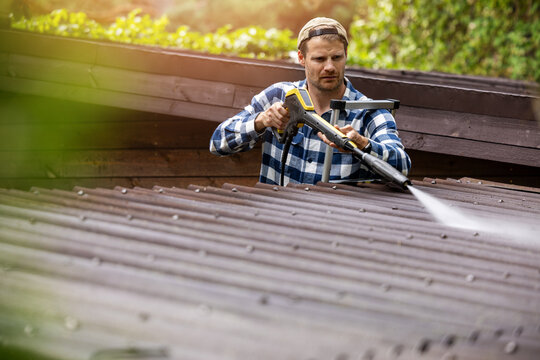 Man washing corrugated roofing sheets with high pressure washer. Roof cleaning service