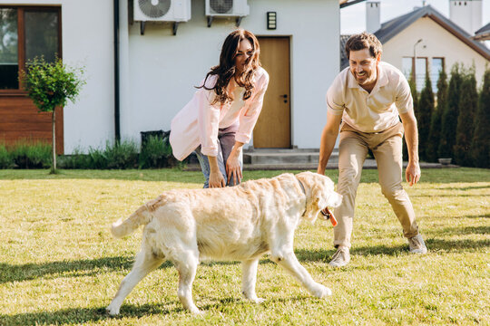 Couple playing with golden retriever in front yard